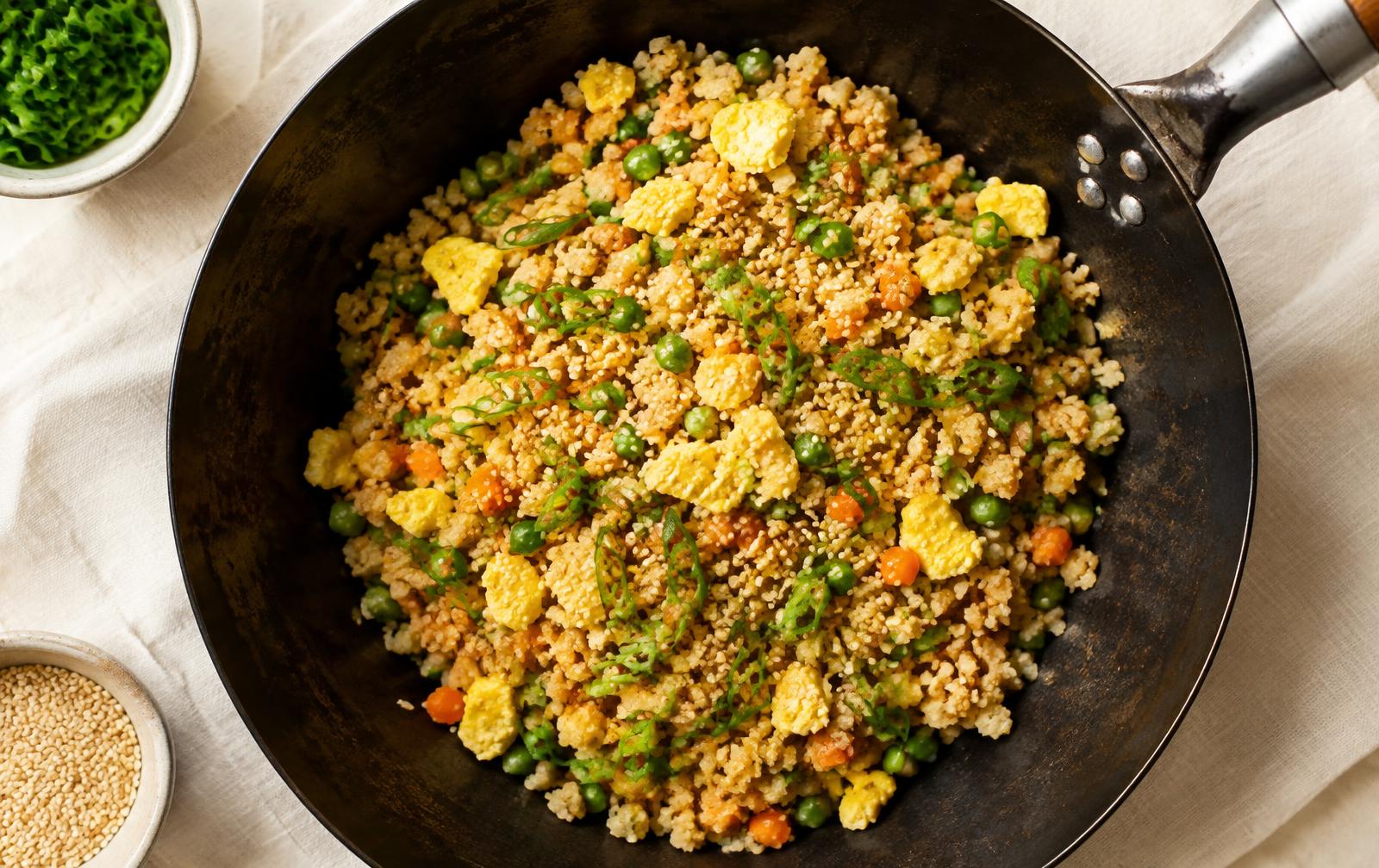 Golden cauliflower fried rice with scrambled egg, peas, carrots, scallions and sesame seeds in a black carbon steel wok