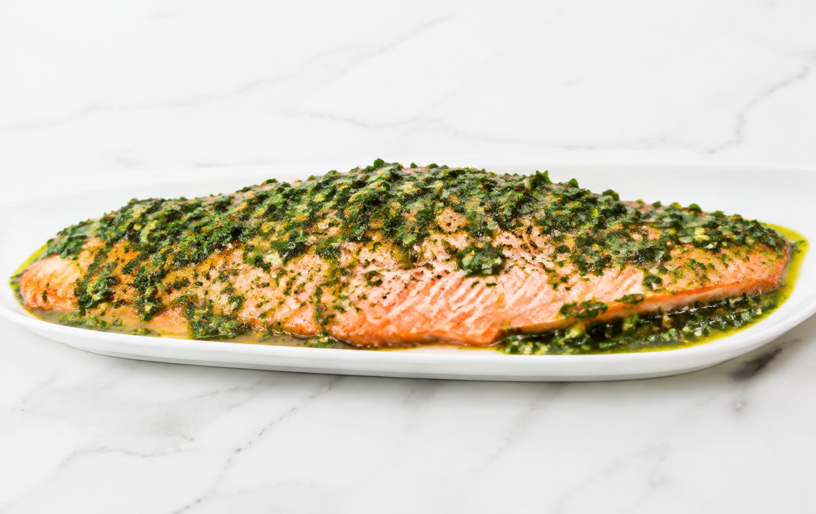 A whole side of slow-roasted salmon topped with bright green salsa verde on a long white platter