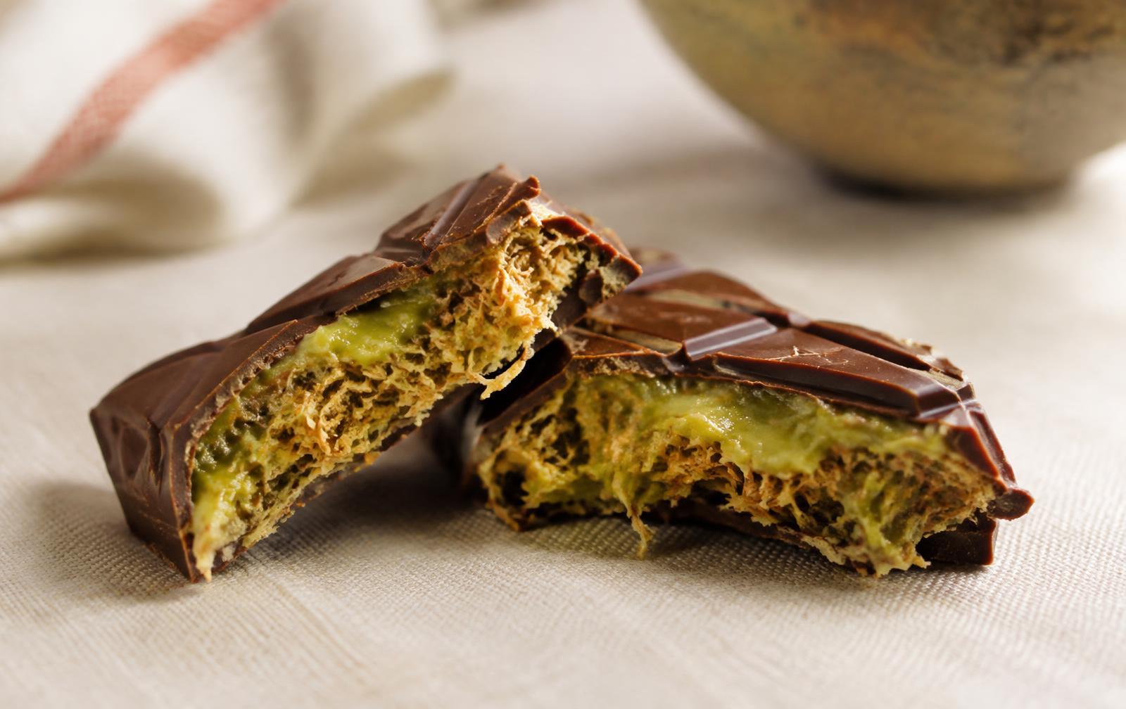 A thick milk chocolate bar broken in half, showing a green pistachio cream and crispy shredded kataifi pastry filling