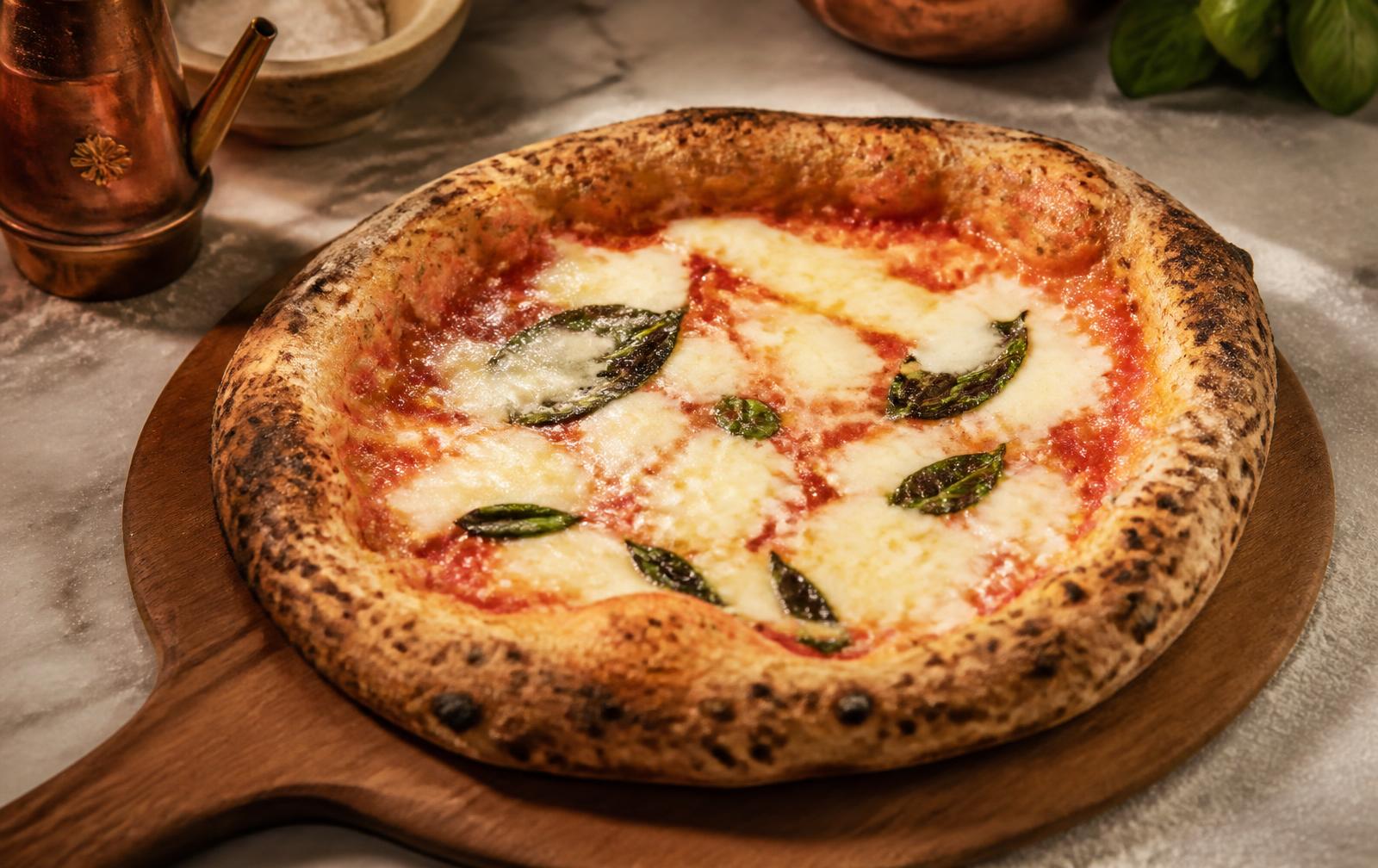 A finished Neapolitan margherita pizza with a puffed leopard-spotted crust on a wooden peel dusted with flour