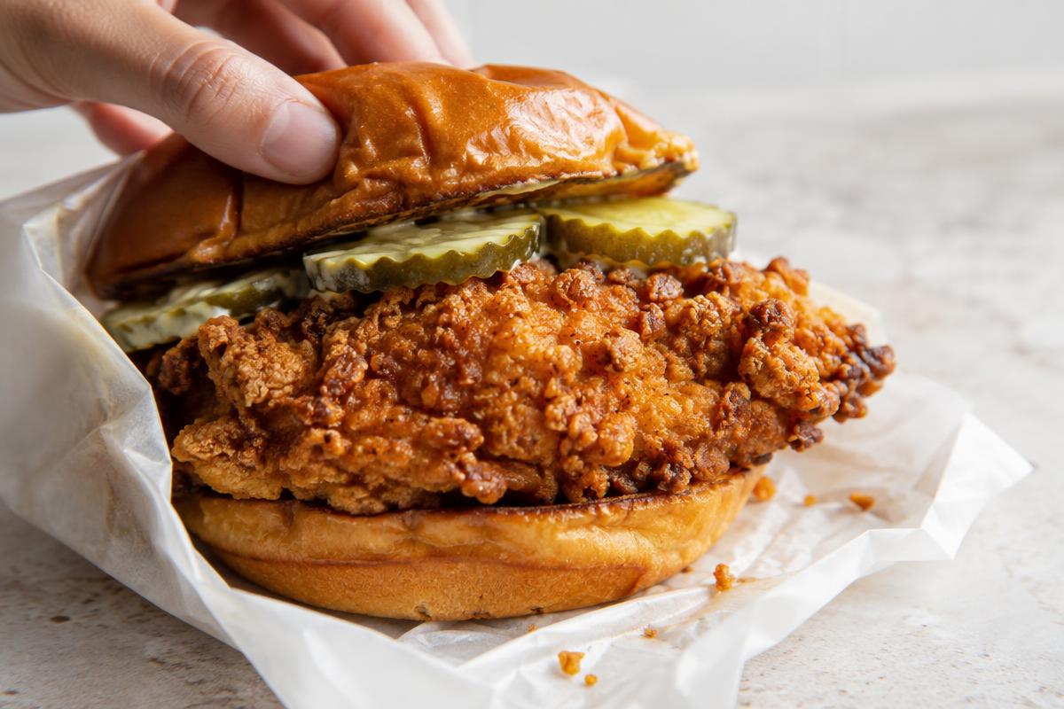 A fried chicken sandwich on a brioche bun with pickles, showing the craggy crust