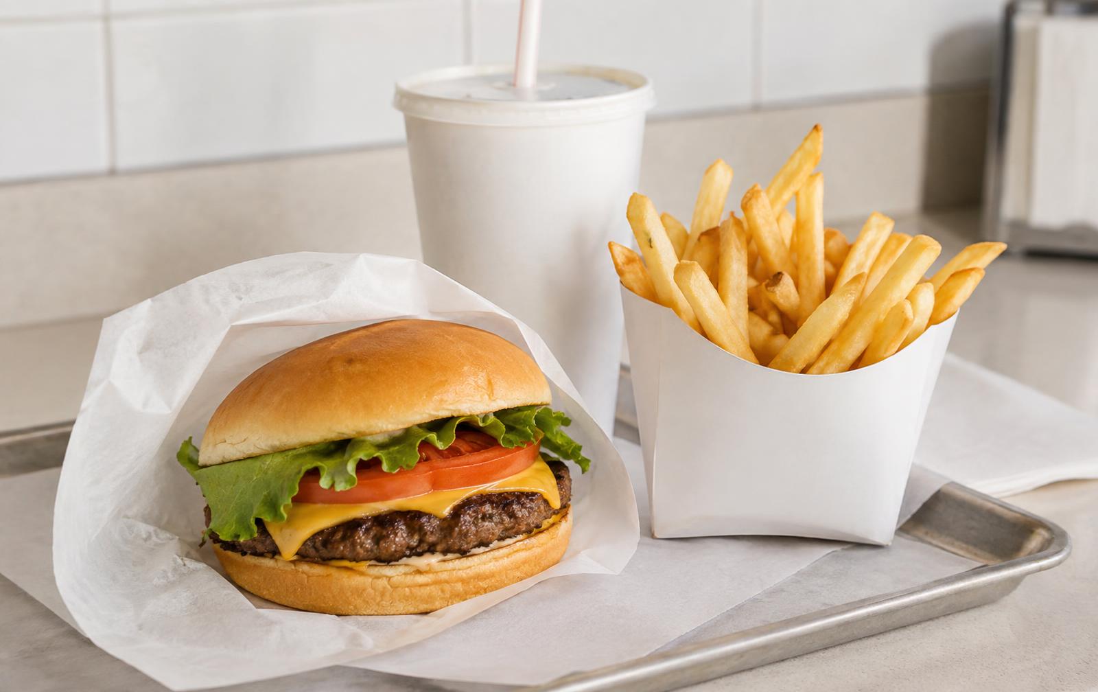 A plain fast food tray with a wrapped cheeseburger, a carton of fries and a paper cup