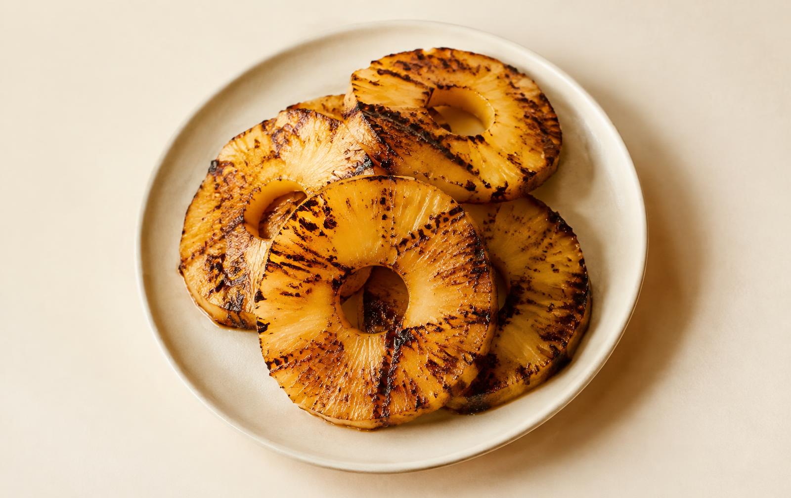 Grilled pineapple rings with dark caramelized char marks on a cream plate