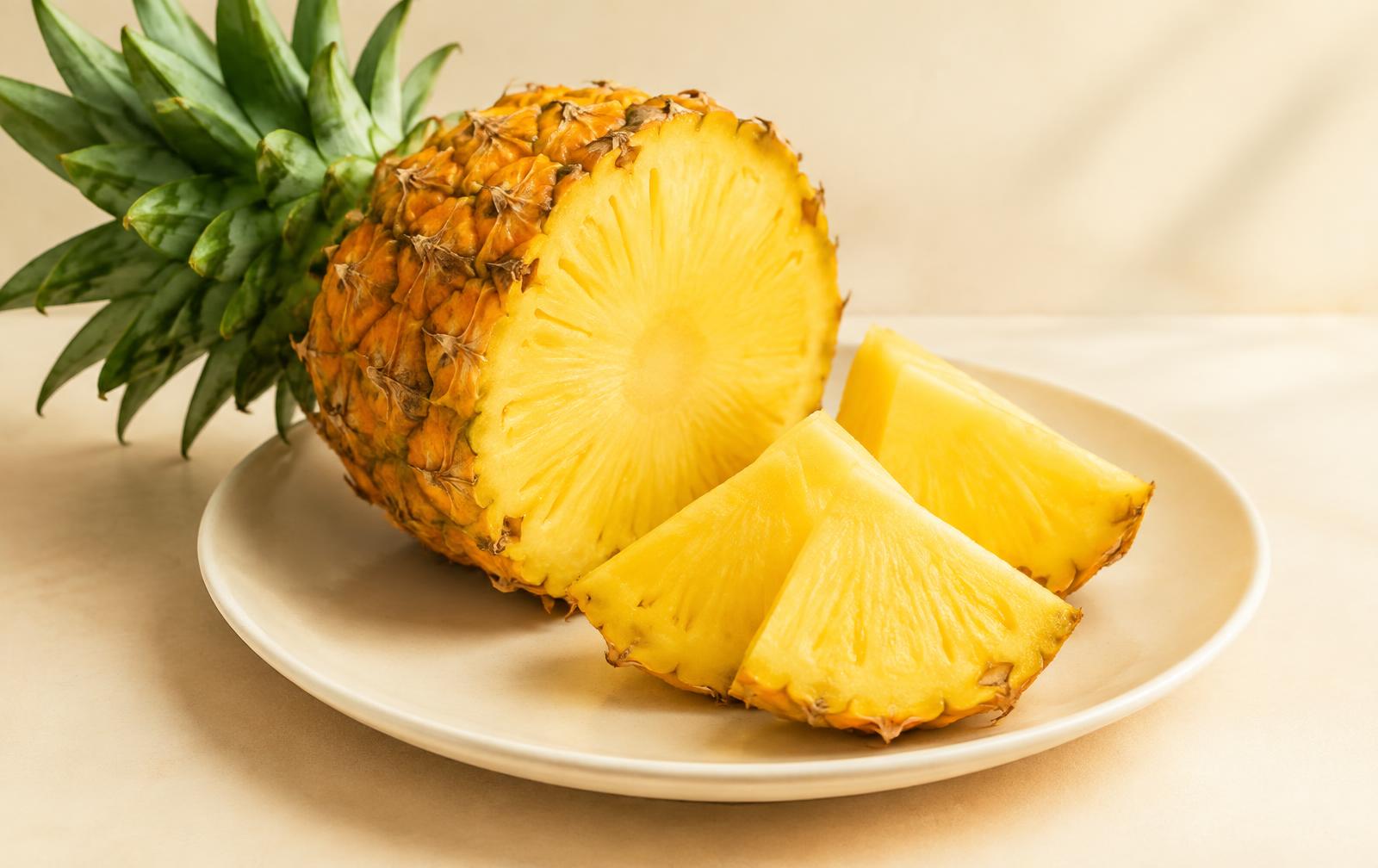 A ripe golden pineapple cut open next to juicy yellow wedges on a cream plate