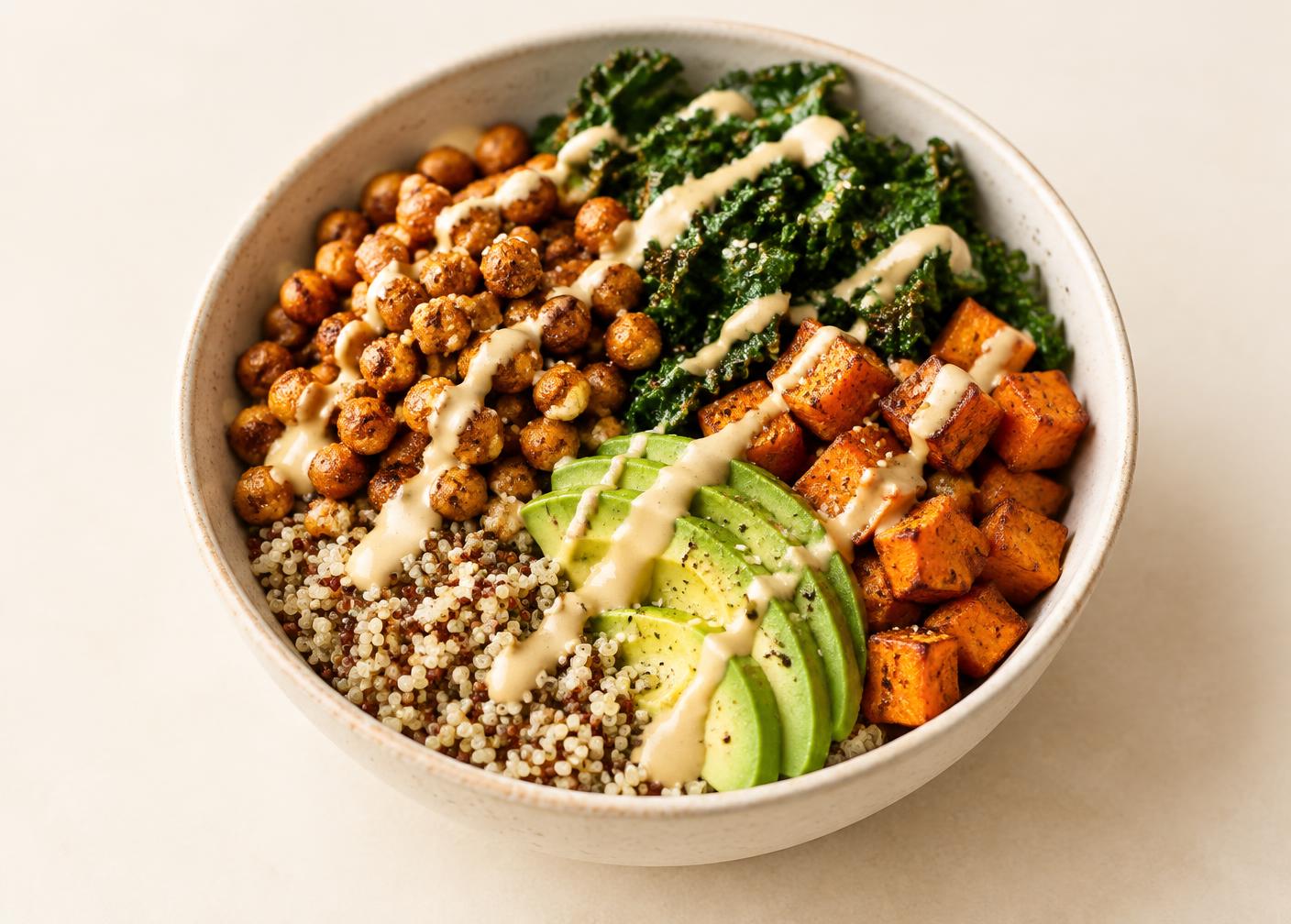 A vegan grain bowl with quinoa, roasted chickpeas, kale, roasted sweet potato and avocado drizzled with tahini